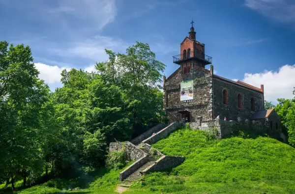 Kamienny kościół na wzgórzu, z kamiennymi schodami prowadzącymi do wejścia. Wokół bujna zieleń, idealne miejsce na odkrywanie dzierżoniów atrakcje.