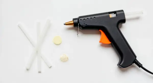 Czarny pistolet do kleju na gorąco z pomarańczowym spustem i kilkoma pałeczkami kleju obok. Dowiedz się, jak włożyć klej do pistoletu.