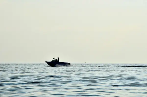 Due persone su un'imbarcazione con potenti motori marini navigano su un mare calmo, lasciando una scia d'acqua.