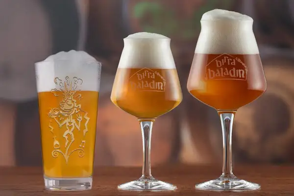 Tre bicchieri di birra, uno tipo pinta americana, con schiuma abbondante e logo Baladin inciso.