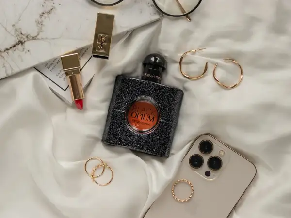 Elegancka kompozycja z flakonem perfum **black opium**, złotą szminką, pierścionkami i telefonem.