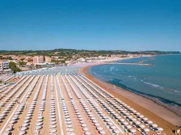 Fano mare: file ordinate di ombrelloni bianchi e colorati sulla sabbia dorata, con il mare azzurro e la costa sullo sfondo.