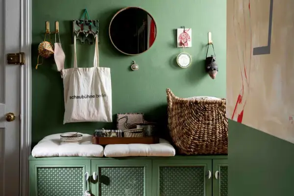 Charming apartment entryway ideas: green cabinet with cushions, tote bag, mirror, and woven basket.