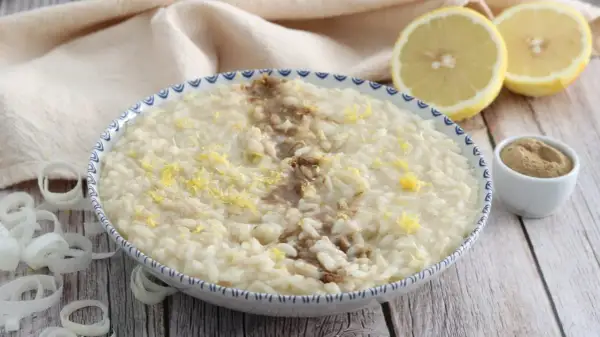 Un cremoso risotto alla liquirizia, guarnito con scorza di limone e una spolverata di polvere scura, pronto per essere gustato.