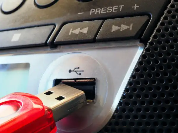 Czerwony pendrive podłączony do portu USB urządzenia. Widoczne przyciski sterowania i głośnik. Parowanie danych z pamięci przenośnej.