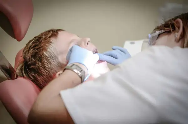 Chłopiec u dentysty, który bada jego usta. Może to być spowodowane bólem podniebienia przy zębach górnych.