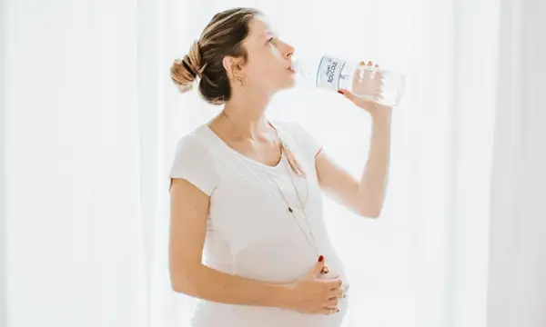 Une femme enceinte boit de l'eau d'une bouteille, prenant soin de son hydratation.