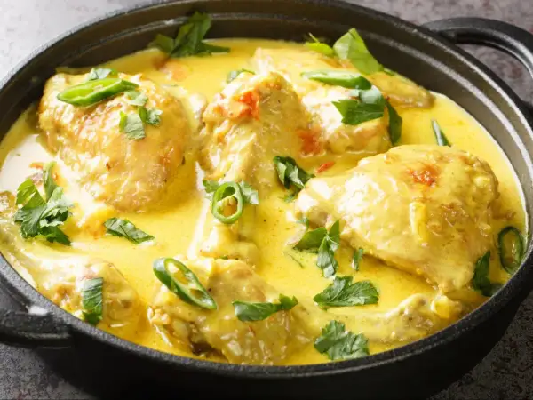 Aksamitny kurczak w mleku kokosowym, udekorowany świeżą kolendrą i plasterkami chili, podany w czarnym naczyniu.