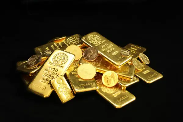 Złote sztabki i monety, w tym słynny Krugerrand, błyszczą na czarnym tle.