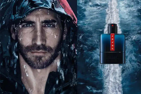Mężczyzna z kroplami wody na twarzy obok butelki perfum Prada Luna Rossa Ocean.