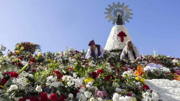 Ofrenda de flores a la Virgen del Pilar. Hombres colocan flores en una estructura adornada con la imagen de la Virgen.
