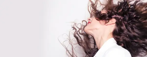 Frauenkopf mit wallenden, braunen Locken, die sich im Wind bewegen. Tipps, wie man locken richtig pflegt, um diesen Schwung zu erhalten.
