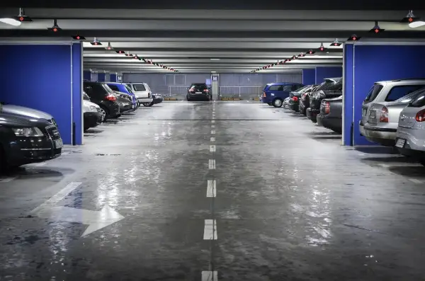 Wielopoziomowy plac postojowy, gdzie mokra podłoga parkingu odbija światła.