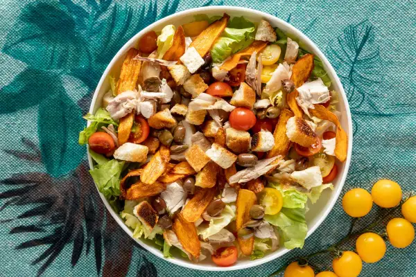 Insalata di pollo ricca con crostini dorati, pomodorini succosi, olive e patate dolci croccanti. Un piatto gustoso e colorato.