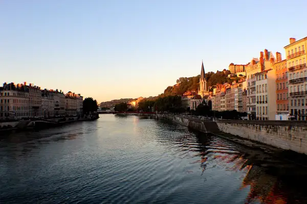 Vue de Lyon au coucher du soleil, avec le Rhône et ses quais bordés d'immeubles. La descente du Rhône offre un spectacle paisible.