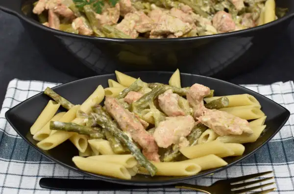 Penne z kurczakiem i szparagami w kremowym sosie. Pyszne danie na talerzu i w garnku.
