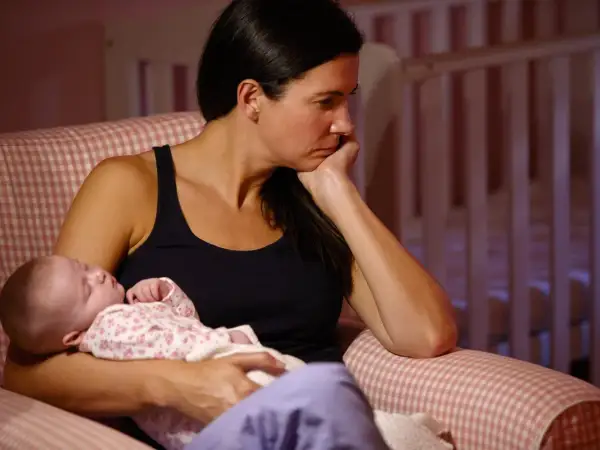 Eine Frau sitzt nachdenklich mit ihrem Baby im Arm. Die Szene deutet auf postnatale Depression hin, eine schwere Zeit für viele Mütter.