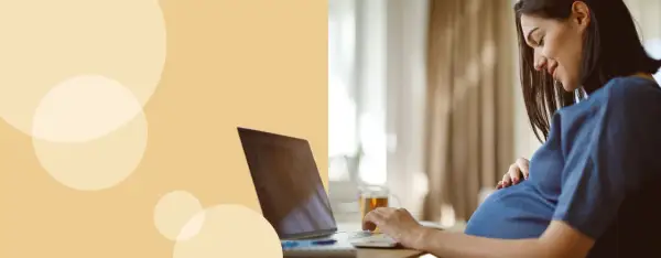 Kobieta w ciąży przy laptopie, która uśmiecha się, dotykając brzucha. Dowiaduje się, jak liczyć ruchy dziecka.