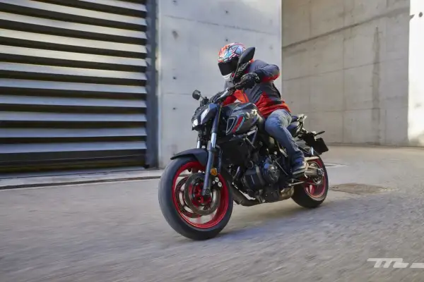 Motociclista con casco y chaqueta roja y gris conduce una Yamaha MT-07 negra con detalles rojos por una calle urbana.