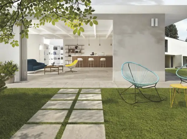 Modern patio with stone pavers, grass, and outdoor seating, opening to a bright, open-plan living and kitchen area.