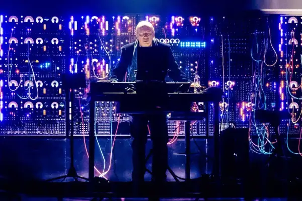 Hans Zimmer stoi przy syntezatorze na tle ściany pełnej migających świateł i kabli.