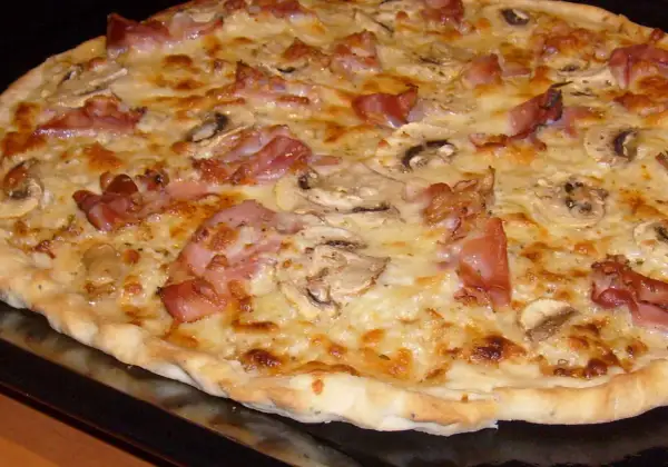 Pyszna pizza carbonara z chrupiącym boczkiem i pieczarkami, obficie posypana serem.