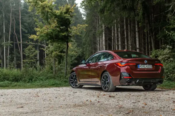 Ciemnoczerwone BMW Gran Coupé na szutrowej drodze w lesie.