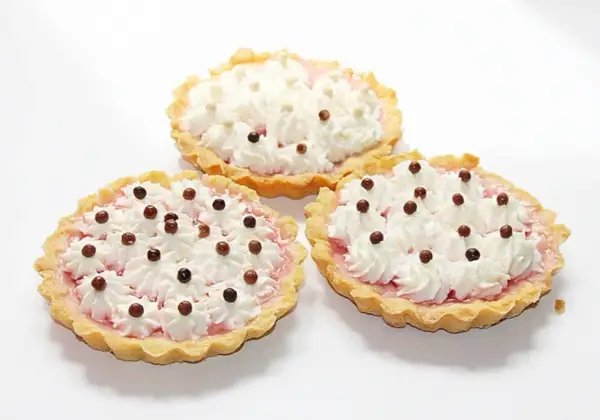 Trzy apetyczne tartaletki z owocami i galaretką, ozdobione bitą śmietaną i czekoladowymi kuleczkami.