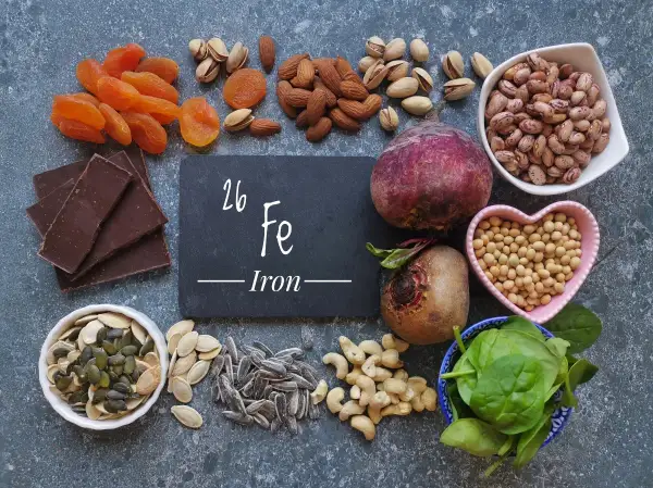 Una tavola ricca di alimenti ricchi di ferro: cioccolato fondente, albicocche, mandorle, pistacchi, barbabietole, fagioli, soia, spinaci, semi di zucca e girasole.