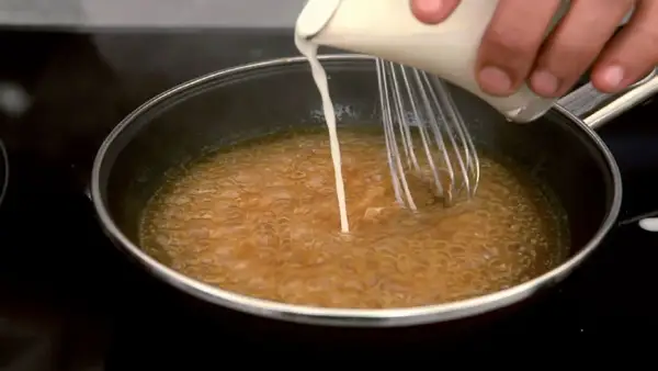 Se añade líquido a una salsa burbujeante en una sartén mientras se bate, para espesar salsa con maicena.