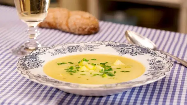 Eine cremige Zucchini-Suppe mit frischer Petersilie in einer eleganten Schüssel, daneben ein Glas Weißwein und ein Brot.