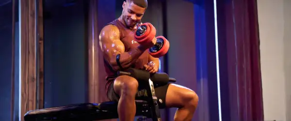 Mann mit Hantel beim Fitness-Training. Schweißglänzende Muskeln, konzentrierter Blick.