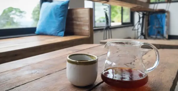 En kaffebryggare i glas med kaffe och en kopp på ett träbord. Perfekt kaffebryggare temperatur för en njutbar stund.