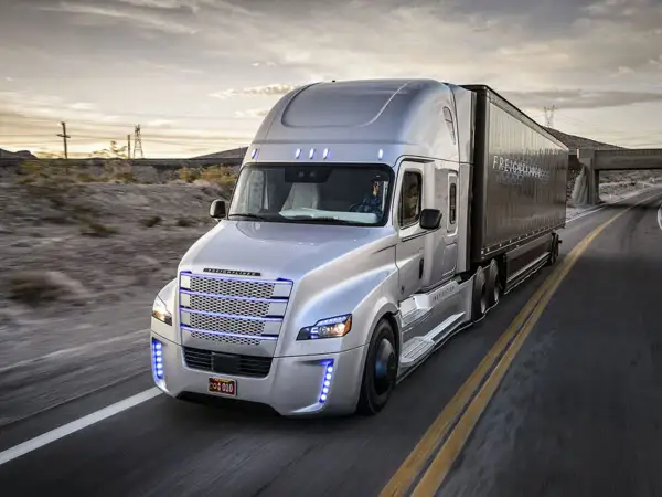Un camion américain nez plat argenté roule sur une route déserte au coucher du soleil.