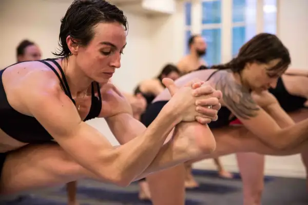 Des pratiquants de hot yoga en pleine concentration, transpirant et étirant leurs corps dans une pièce chauffée.