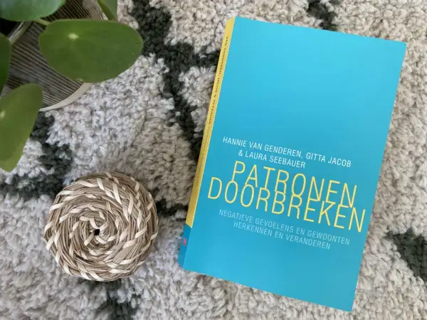 Boek "Patronen doorbreken" op een zachte, getextureerde ondergrond. Een plantje en een mandje liggen ernaast.