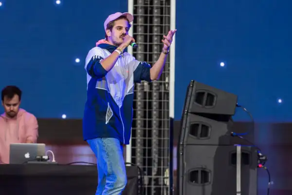 Artysta na scenie, jeden z najpopularniejszych polskich wykonawców pop, śpiewa do mikrofonu. W tle DJ przy laptopie.
