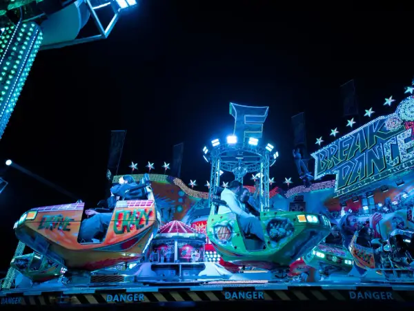 Bunte Fahrgeschäfte und Lichter auf dem Berliner Volksfest. Menschen genießen die Nacht auf dem "Break Dance".