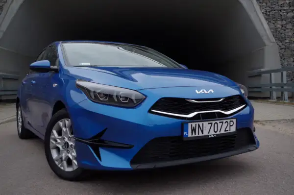 Niebieska Kia Ceed 1.5 T-GDI z nowoczesnymi światłami i grillem, zaparkowana przy betonowym tunelu.