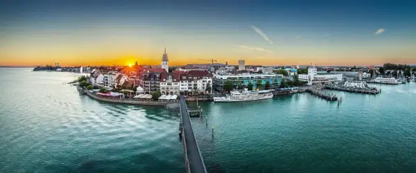 Friedrichshafen heute: Sonnenuntergang über dem Bodensee, mit Schiffen im Hafen und der Promenade.