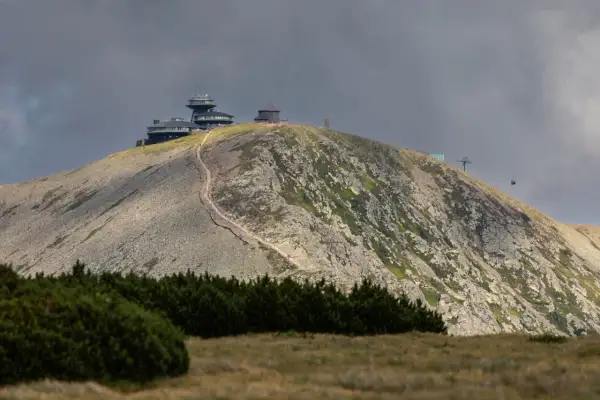 Kamienna ścieżka prowadzi na szczyt Śnieżki, gdzie widać budynki obserwatorium i kolejkę linową.