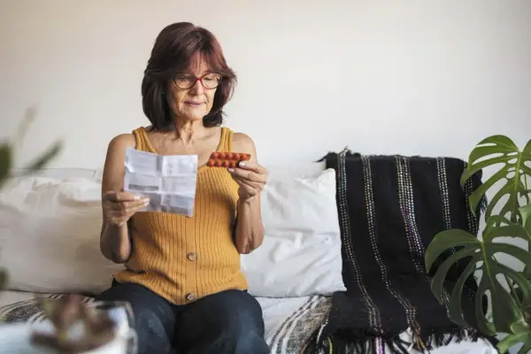 Kobieta czyta ulotkę leku, trzymając opakowanie tabletek. Szuka informacji o lekach na menopauzę bez recepty.