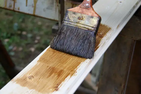 Application d'une lasure blanche sur une planche de bois. Le résultat avant/après est visible sur la surface traitée.