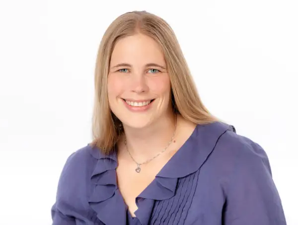 Lächelnde Frau mit blonden Haaren und blauen Augen, trägt eine lila Bluse. Sie könnte eine engagierte studentische Hilfskraft sein.
