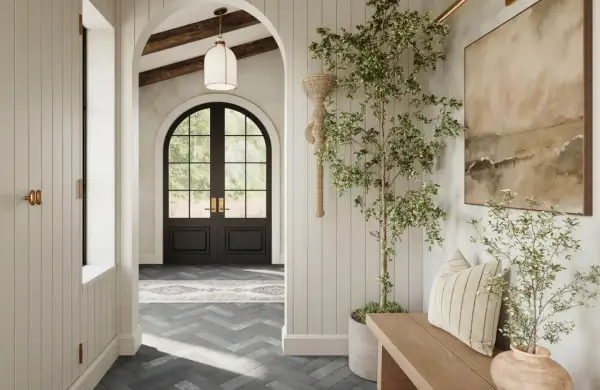 A bright, airy hallway with a dark arched doorway leading outside. A potted tree and bench add warmth to the space.