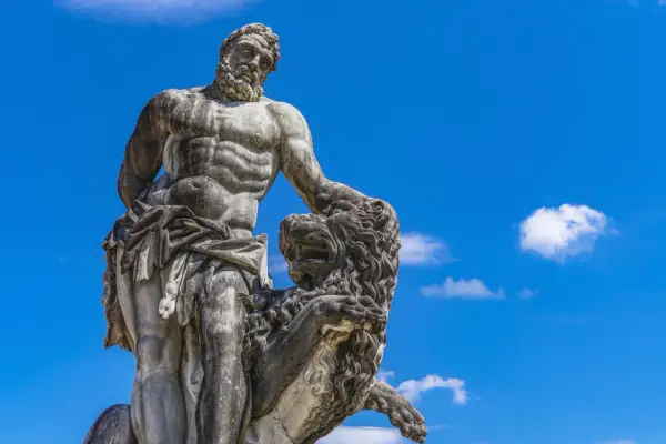 Statue de marbre d'Hercule, dieu grec, luttant contre un lion, sous un ciel bleu éclatant.