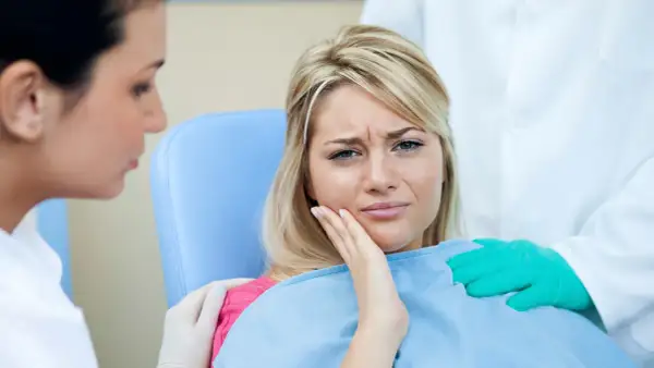 Kobieta cierpi na ból zęba po zatruciu. Dentysta i asystentka próbują jej pomóc.