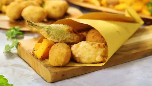 Un cono di carta gialla contiene fritti misti, tra cui spicca una mozzarella in carrozza filante, accompagnata da verdure pastellate e polenta fritta.