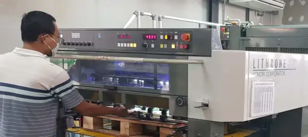 Operator w maszynie drukarskiej Komori Lithrone A37 z panelem sterowania i wyświetlaczem.