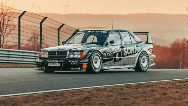 Czarny Mercedes 190 Evo na torze wyścigowym, z licznymi sponsorami na karoserii, gotowy do startu.